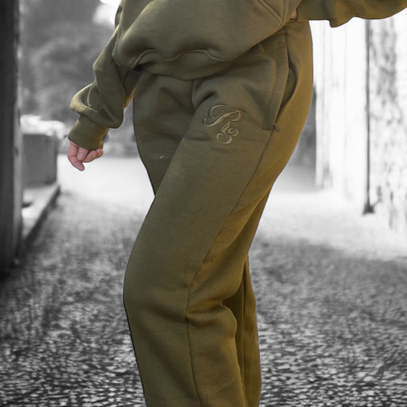 A close-up of a person wearing gray Coz3 Max Unisex Sweatpants, showing the side pocket and the brand's logo on the leg of the pants.