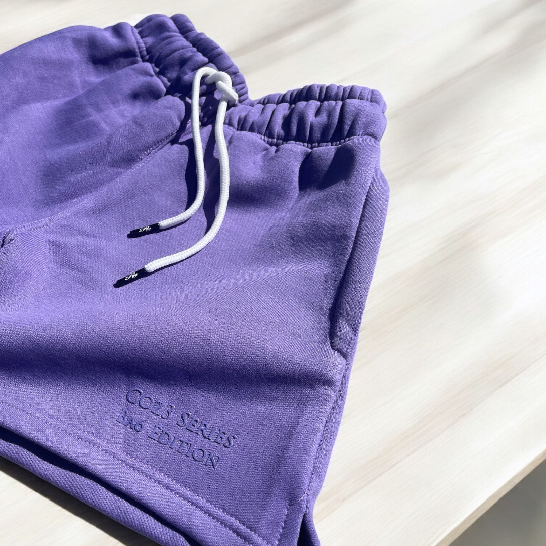 An array of Coz3 Ba6 Edition Shorts in various colors including pink, blue, purple, white, and gray, displayed in a line with a soft focus background. The shorts are characterized by a relaxed fit, 3-inch waistband, and drawstrings.