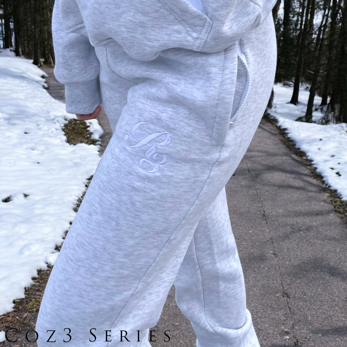 A close-up of a person wearing gray Coz3 Max Unisex Sweatpants, showing the side pocket and the brand&#39;s logo on the leg of the pants.