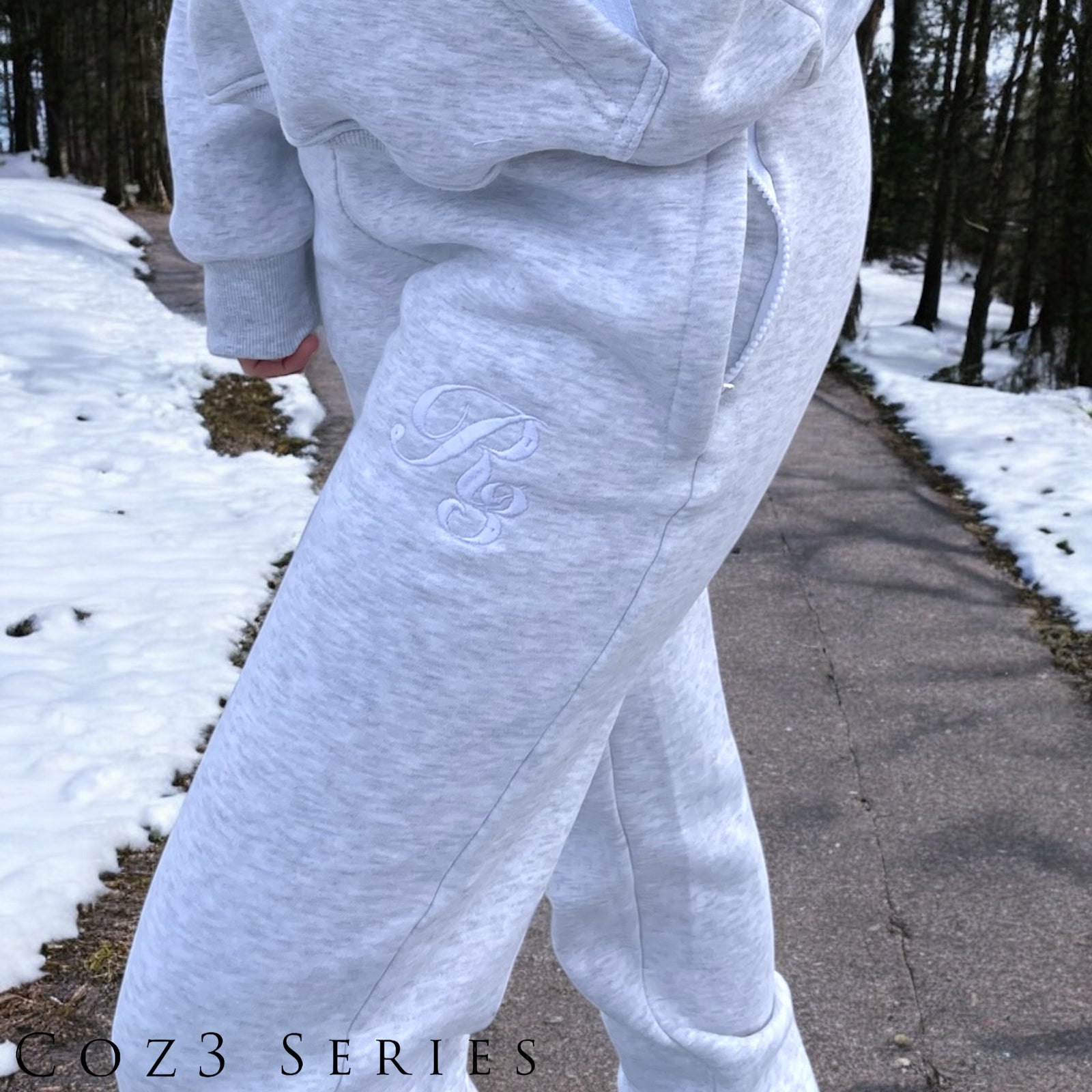 A close-up of a person wearing gray Coz3 Max Unisex Sweatpants, showing the side pocket and the brand's logo on the leg of the pants.